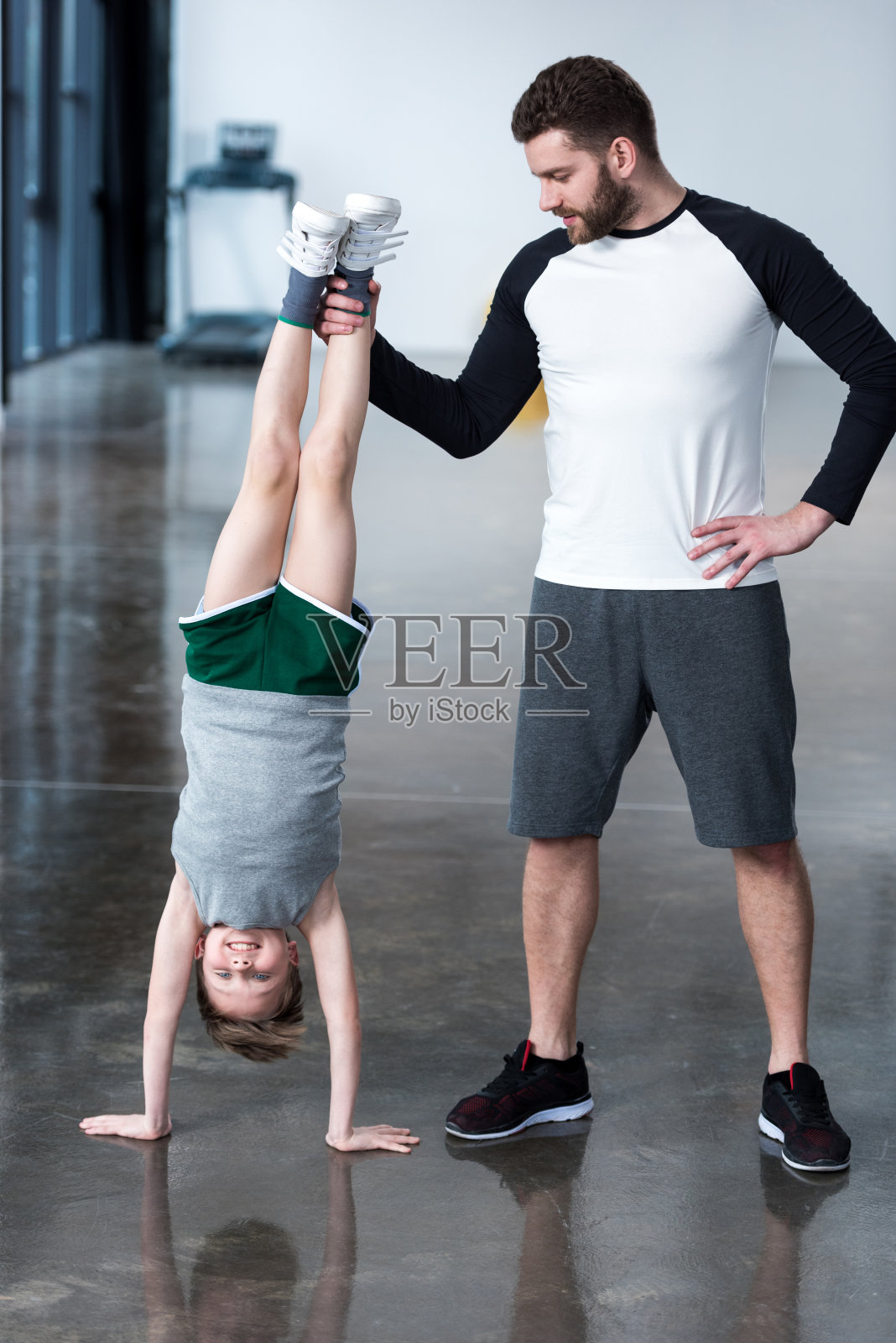 教练在健身室帮助男孩倒立照片摄影图片