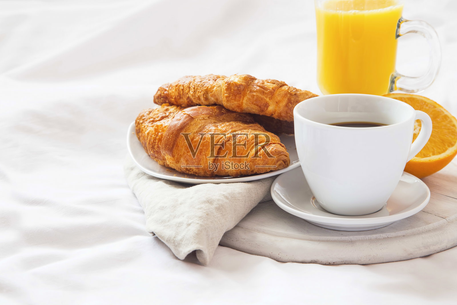 床上早餐，咖啡杯，羊角面包和橙汁放在白床单上照片摄影图片