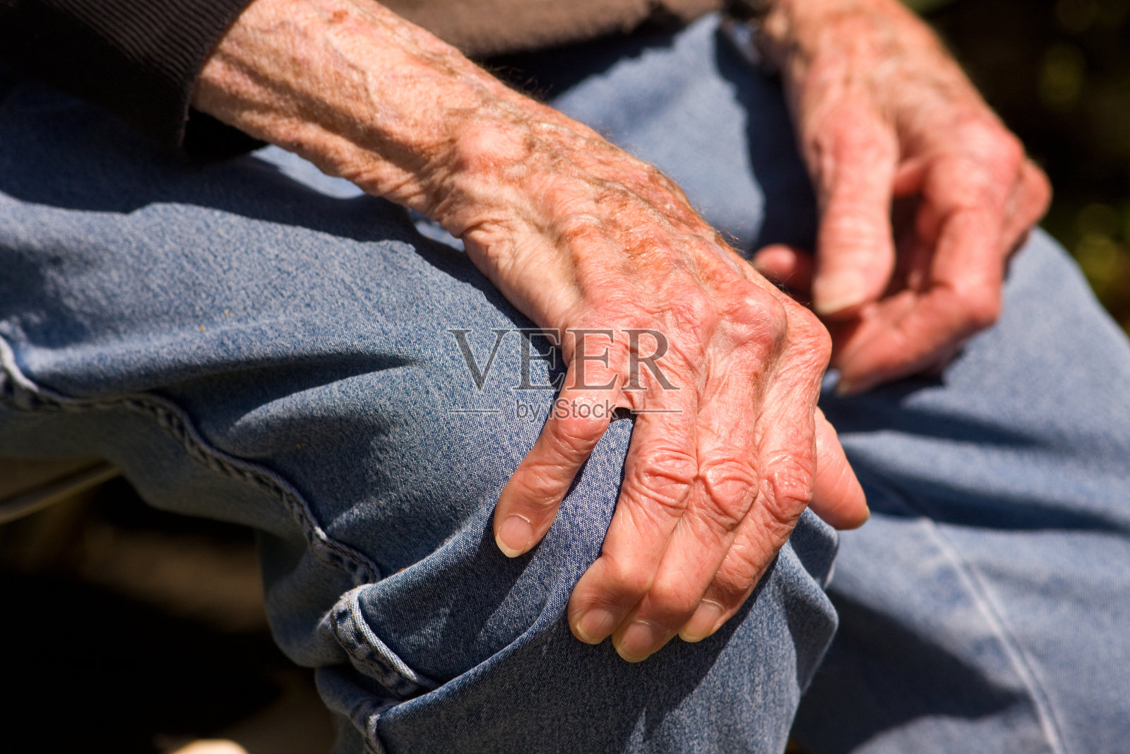 一双老人的手抓住了一个牛仔布包裹的膝盖照片摄影图片