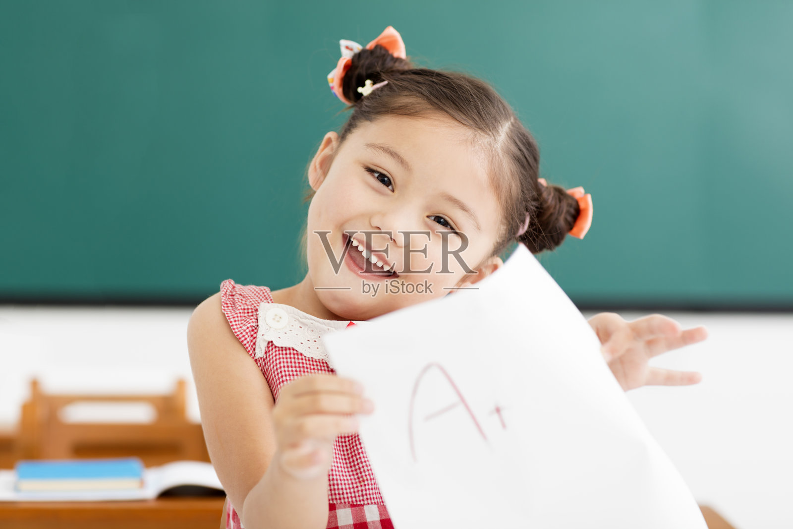 快乐的小女孩在教室里展示着有加分的试卷照片摄影图片