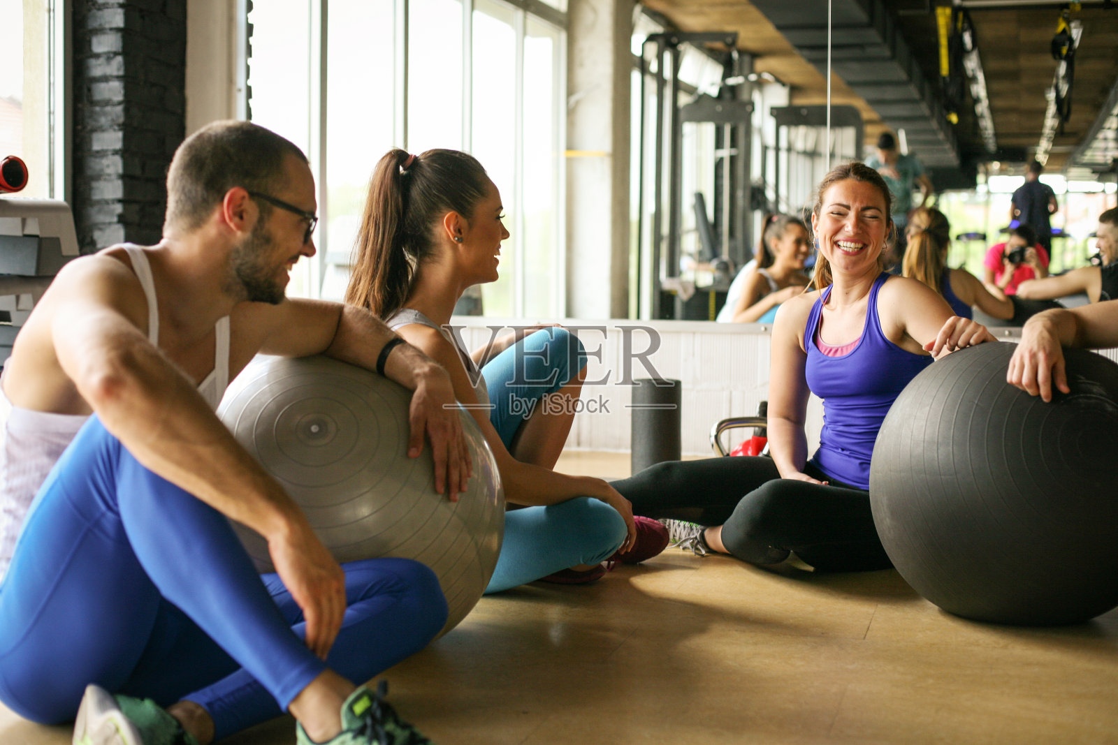 一群人在健康俱乐部锻炼。人们在普拉提运动后用普拉提球交谈。照片摄影图片