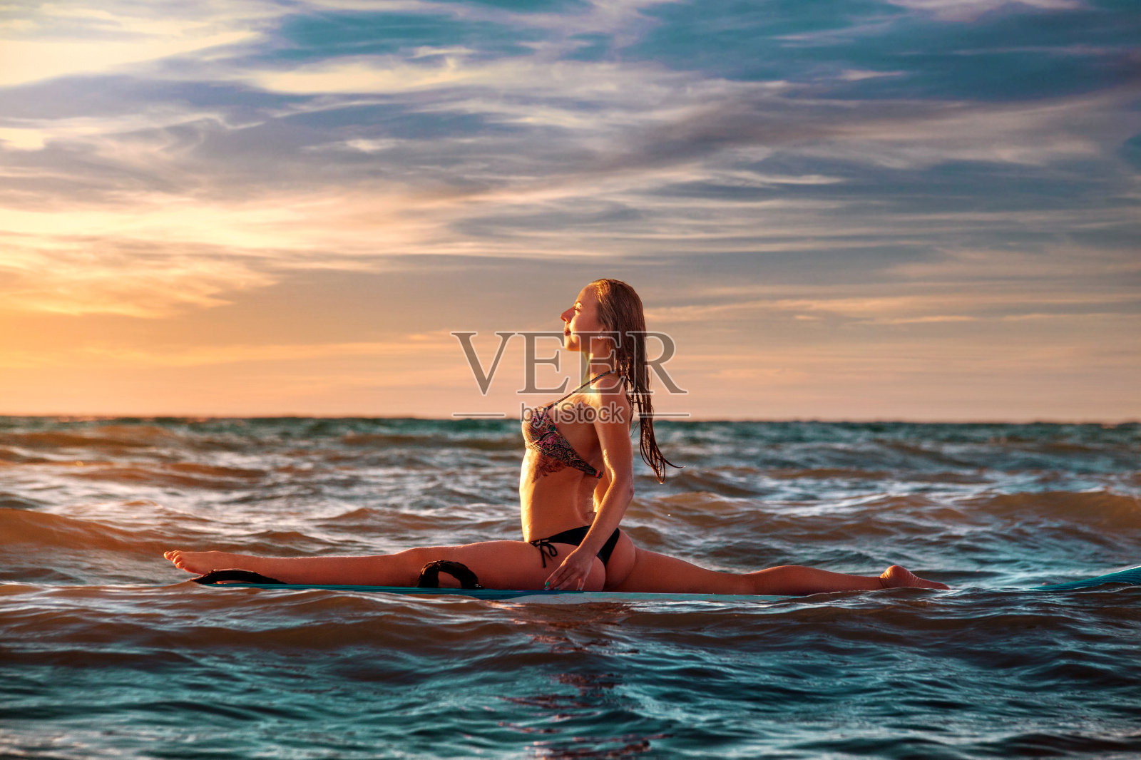 女人练习SUP瑜伽在日落，沉思在一个桨板。照片摄影图片