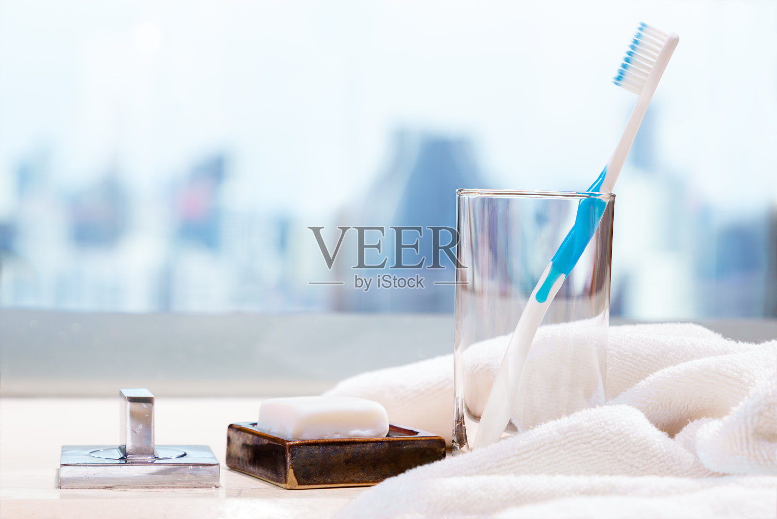 干净的牙刷放在浴室台面的透明玻璃里，白色的肥皂和毛巾，模糊的背景，健康的生活方式的概念，复制或文本的空间照片摄影图片