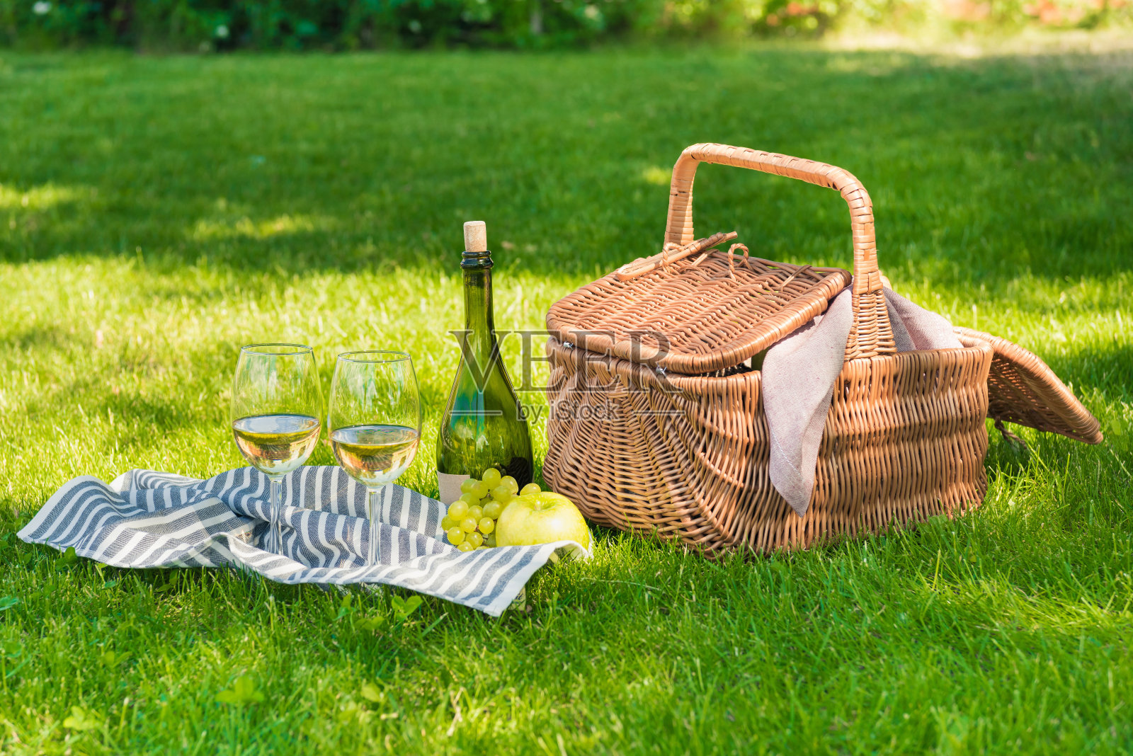 近距离观察柳条野餐篮子，水果和酒瓶与餐巾上的杯子照片摄影图片
