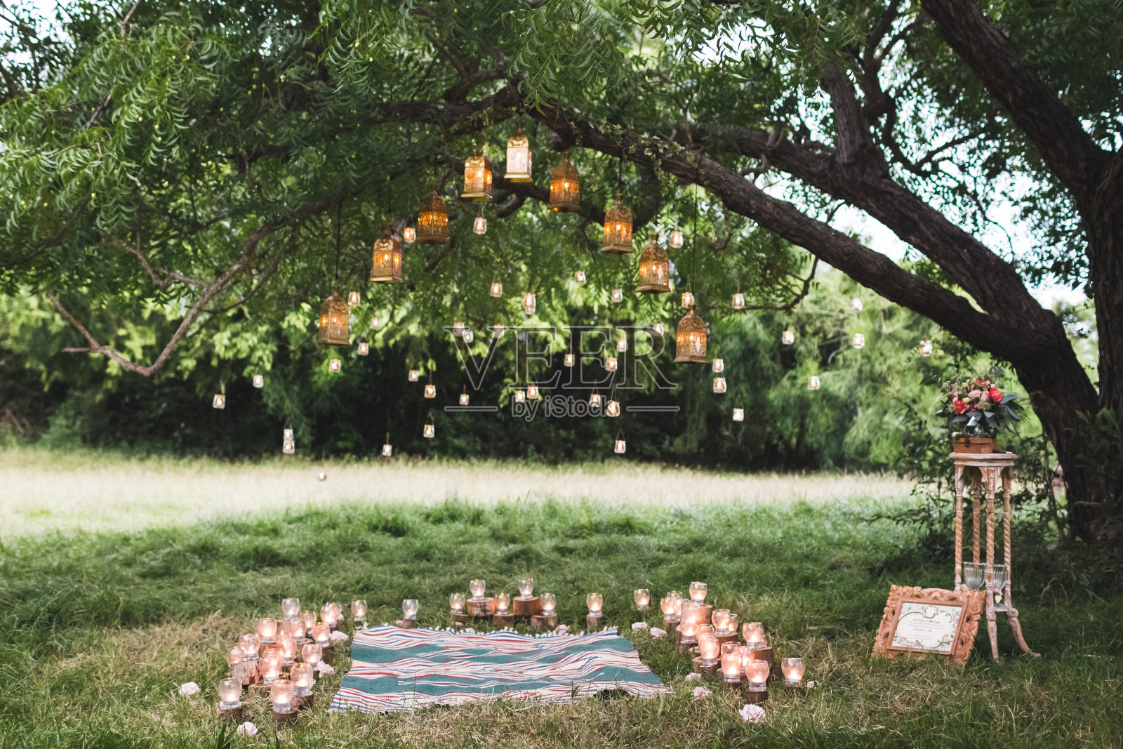 晚上的婚礼上有地毯和许多古董灯和大树上的蜡烛。乡村风格照片摄影图片