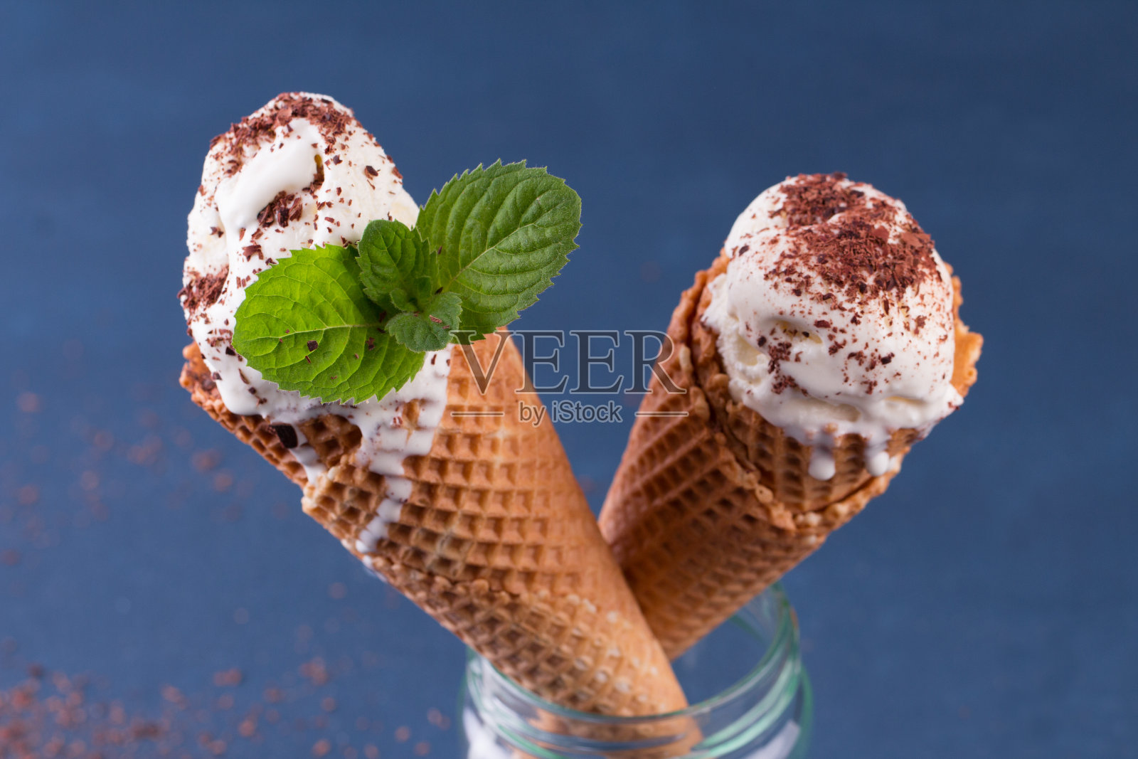 传统的华夫筒冰淇淋在玻璃罐在蓝色的桌子上。装满冰淇淋的蛋卷照片摄影图片