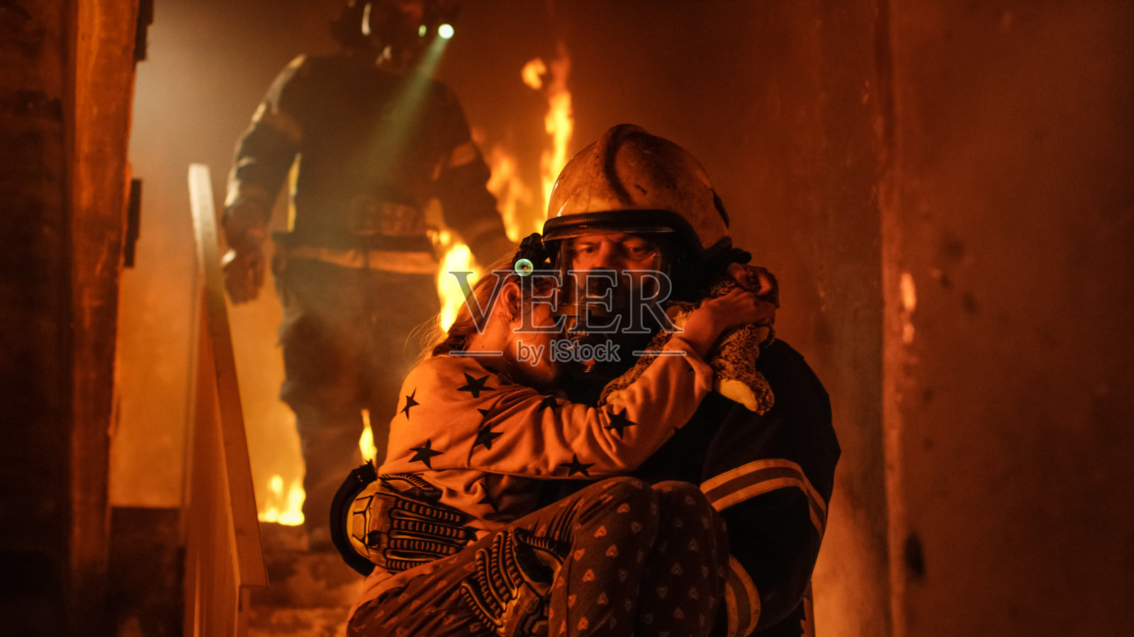 燃烧的大楼。一组消防员从燃烧的楼梯上下来。在前景，一名消防员抱着救下的女孩。照片摄影图片