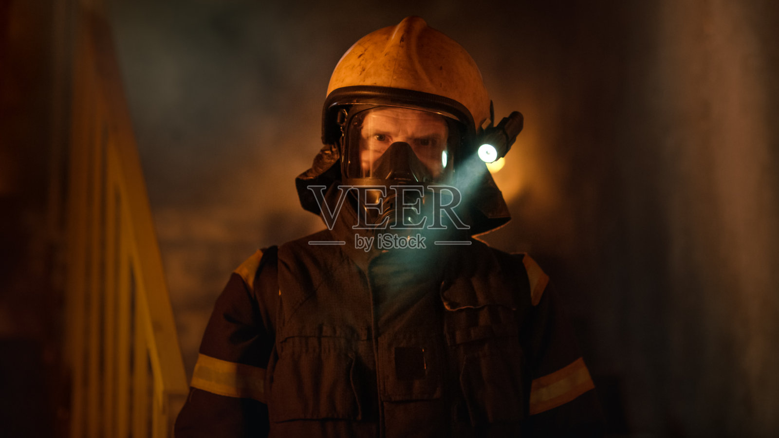 肖像拍摄的一个勇敢的消防员站在一个燃烧的建筑物熊熊大火在他身后。背景中的明火和烟雾。照片摄影图片