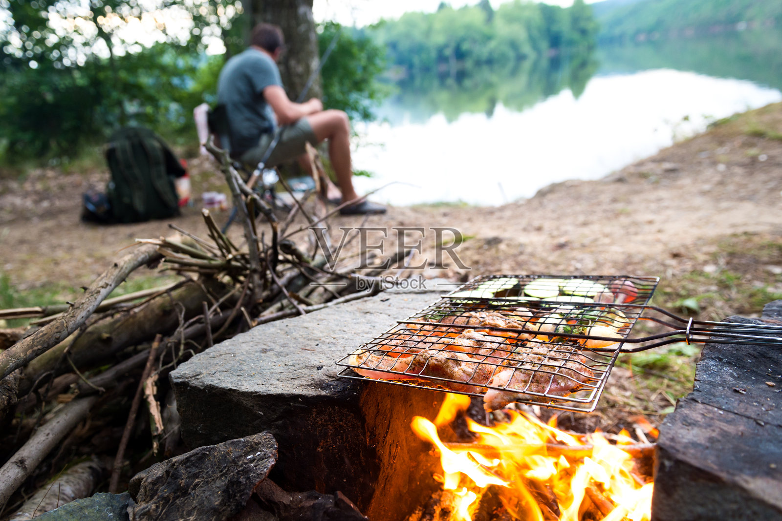渔夫在篝火上准备晚餐，冒险生活方式露营钓鱼的概念照片摄影图片