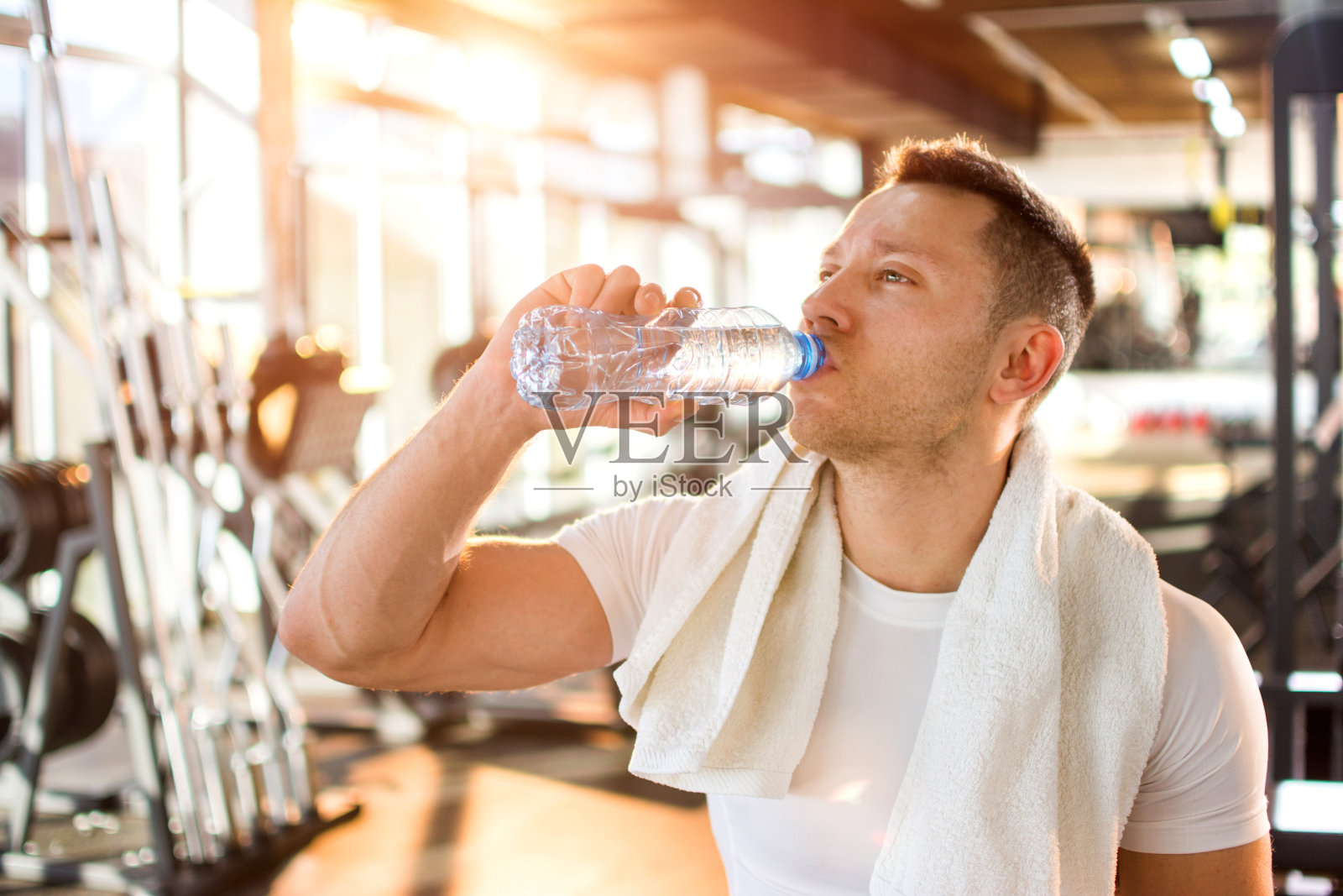 年轻帅气的男子在健身房里喝水的肖像。照片摄影图片