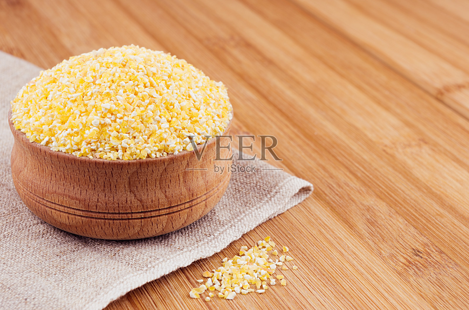 木碗里的玉米粒放在棕色的竹板上，特写。燕麦食品的背景。照片摄影图片