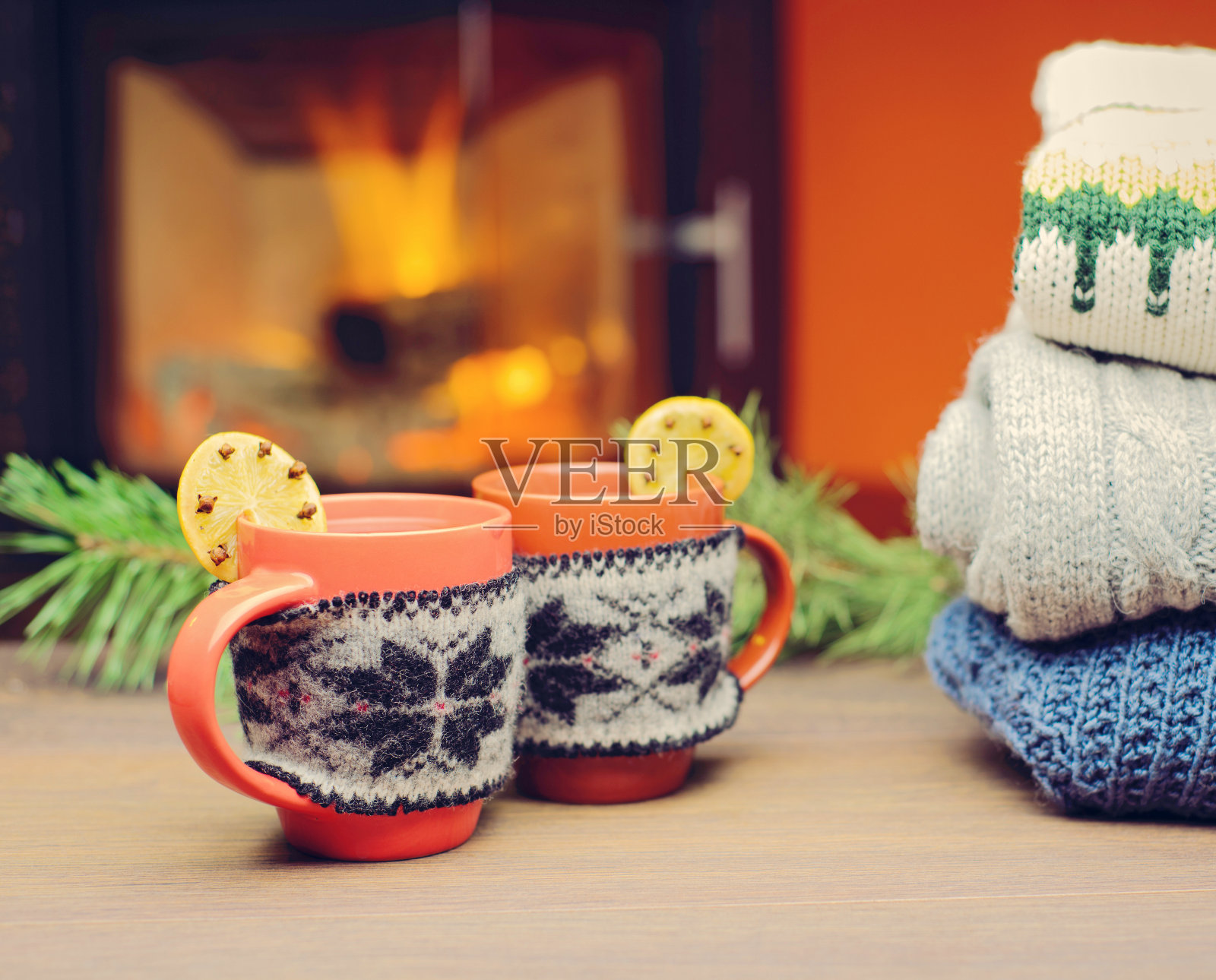 壁炉旁有圣诞装饰的杯子。戴着红色针织手套的马克杯站在炉边。在温暖的壁炉前喝一杯热饮。一堆舒适的针织毛衣。照片摄影图片