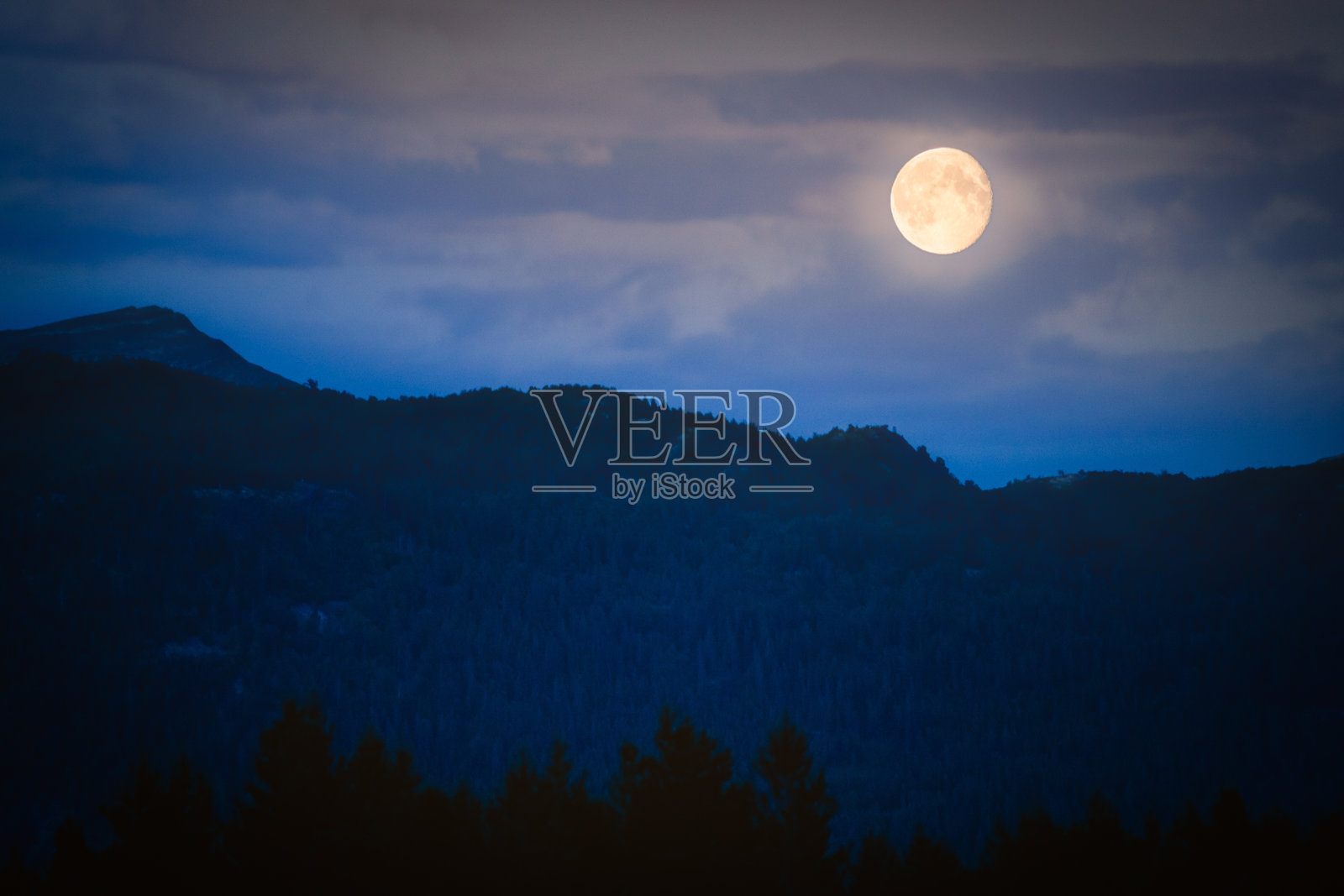 满月在黄昏在黑暗的山与云的背景和森林在前景照片摄影图片