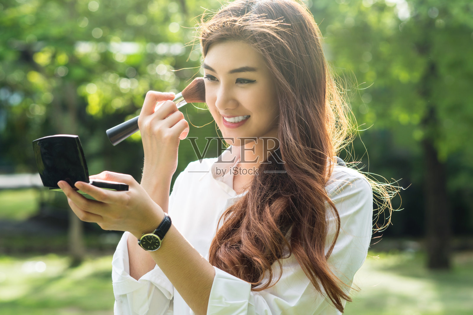 肖像美丽的亚洲年轻女子化妆到她的脸在公园，美丽和时尚的概念照片摄影图片