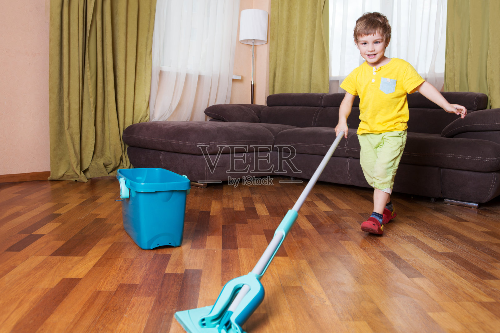 男孩在房间里打扫地板。男孩帮助妈妈打扫卫生。照片摄影图片