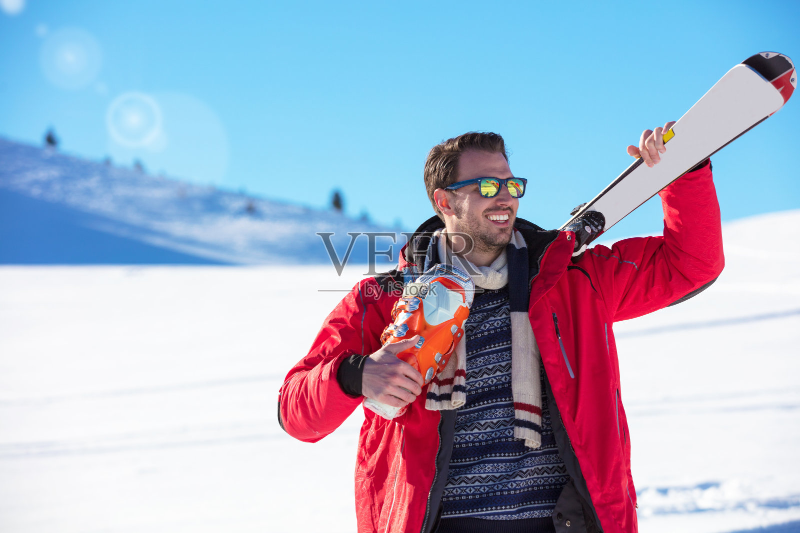 一幅健康男子的肖像，手里拿着一对滑雪板，微笑着望向一边照片摄影图片