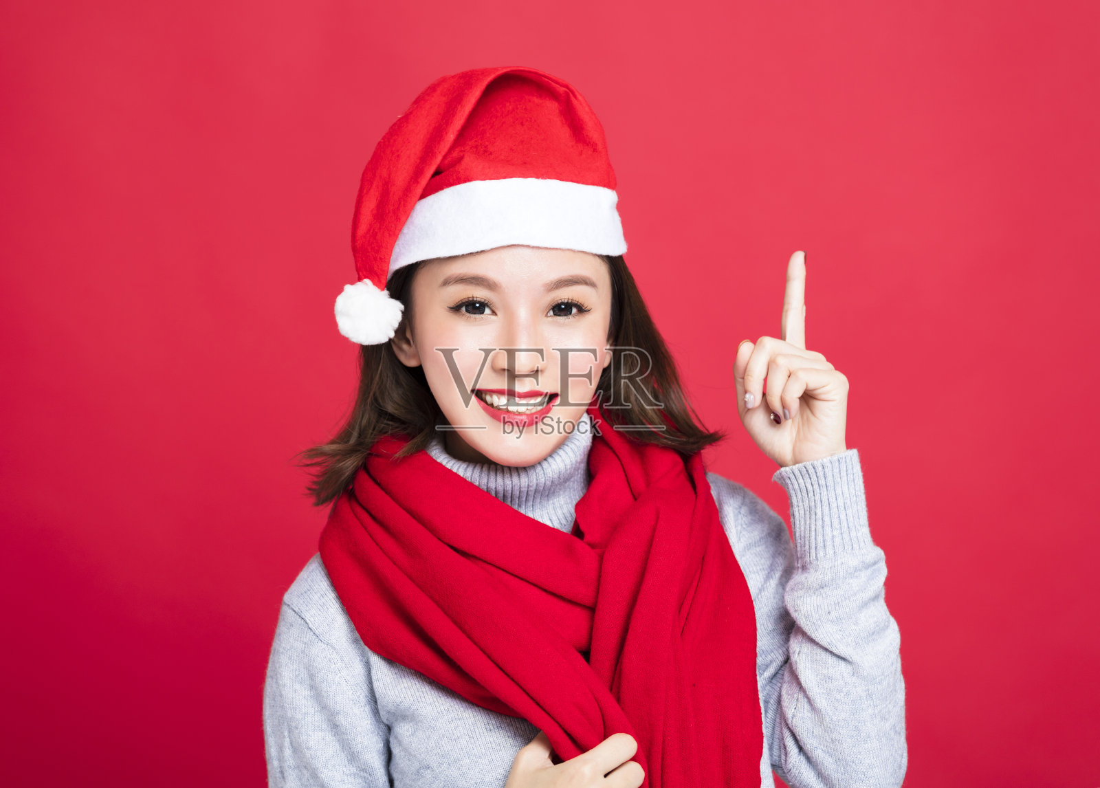 年轻的圣诞妇女戴着圣诞老人帽，指着上面照片摄影图片