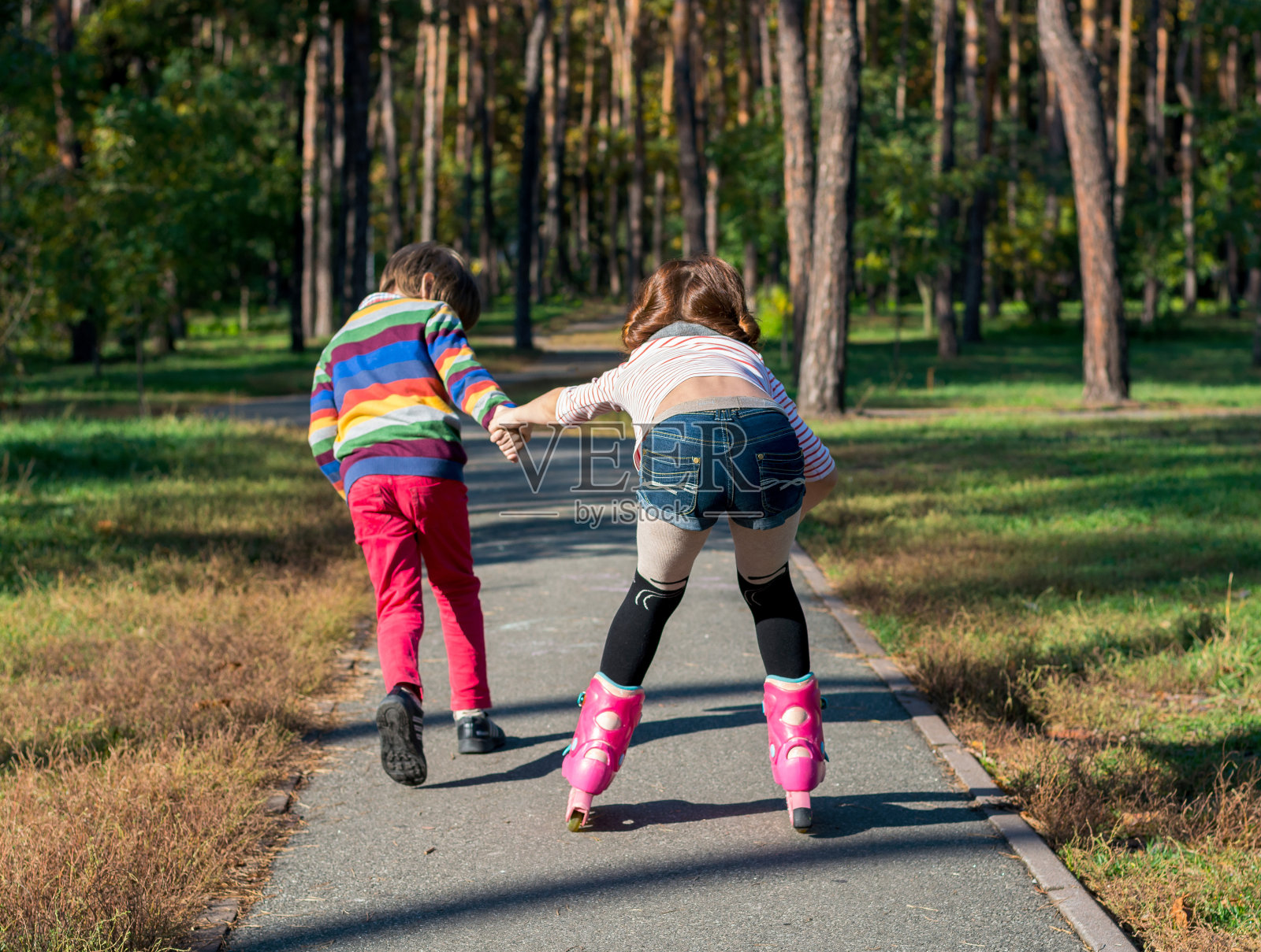 男孩帮助女孩在公园里滑旱冰。照片摄影图片