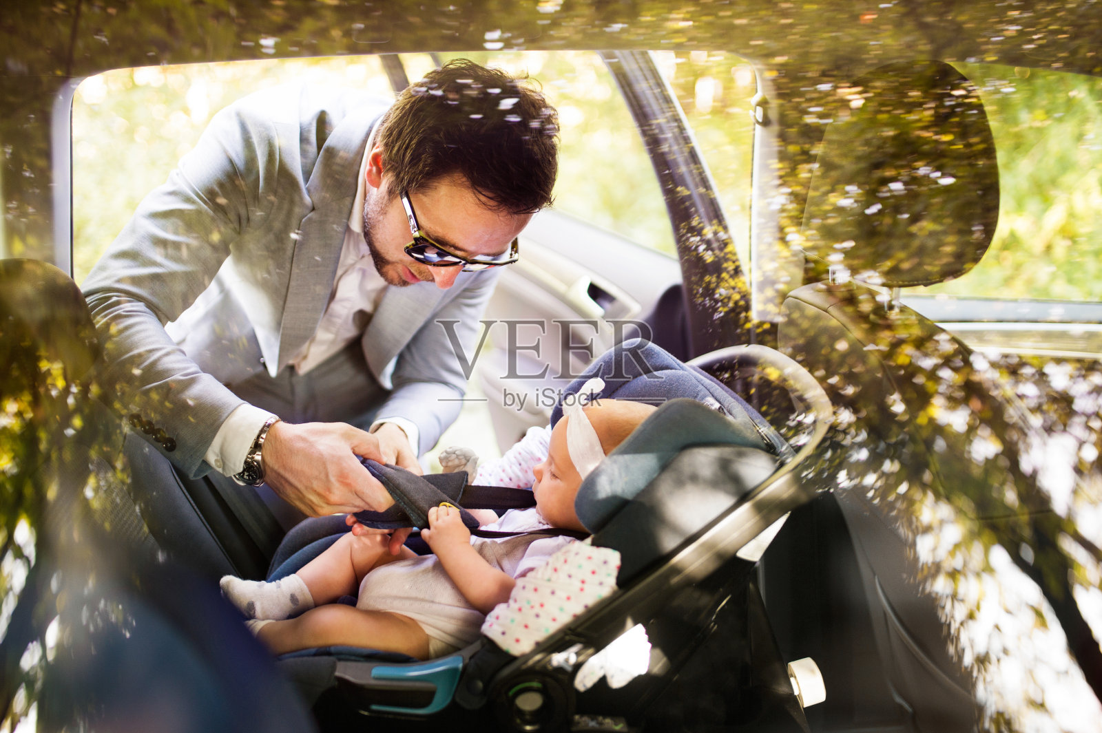 年轻的父亲把女儿放进车里。照片摄影图片