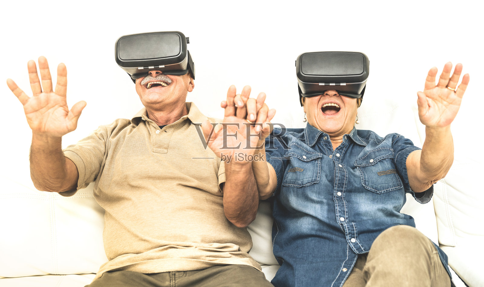 老两口玩得很开心，戴着虚拟现实耳机坐在沙发上-快乐退休的人用现代vr眼镜-新趋势和技术概念和有趣的活跃的老年人照片摄影图片