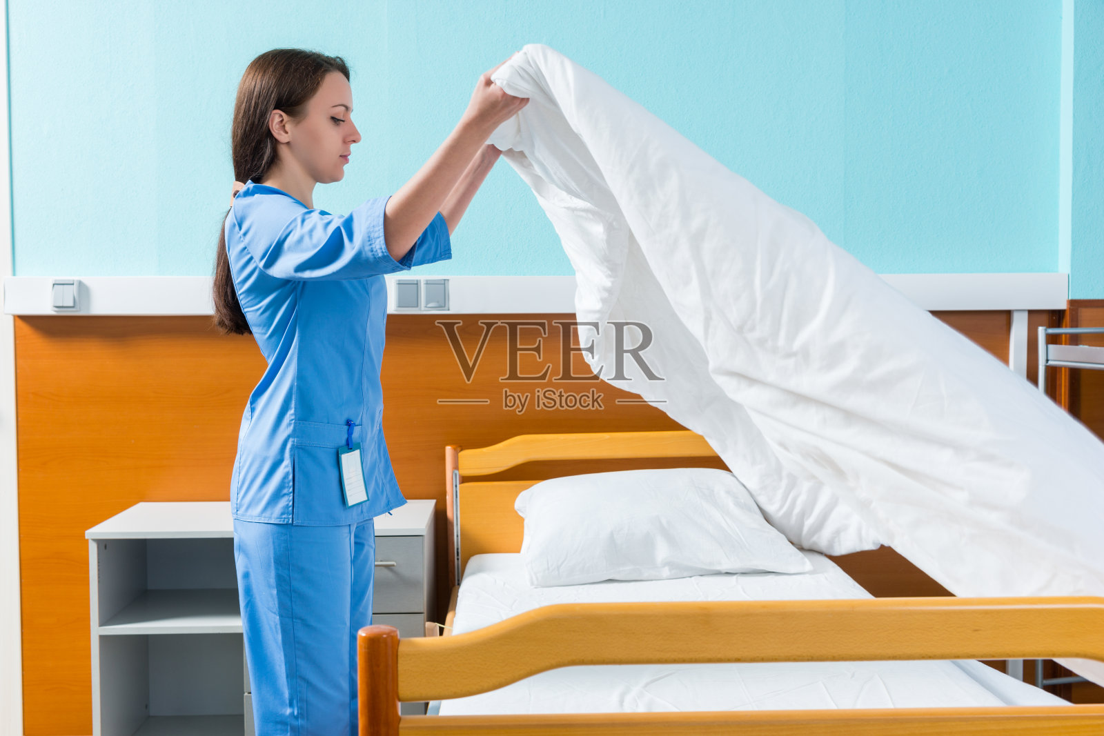 身穿蓝色制服的年轻护士在病床上换床单照片摄影图片