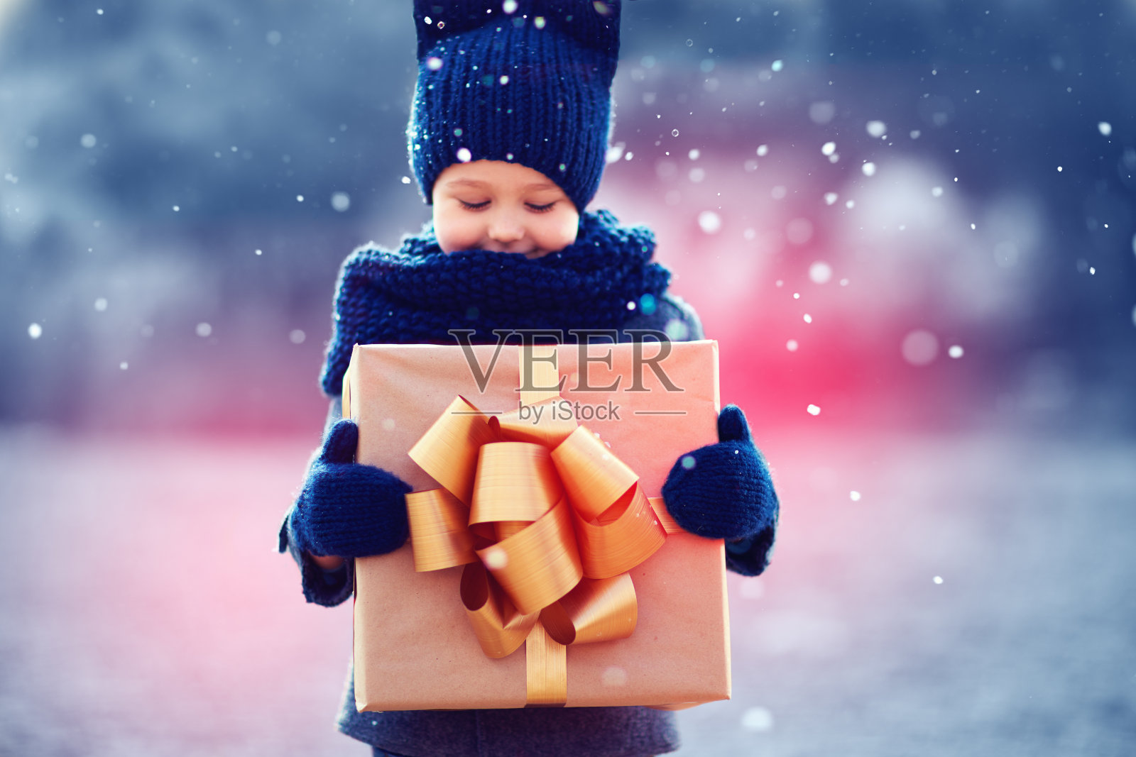 可爱的孩子在大雪下拿着大礼盒。专注于礼品盒照片摄影图片