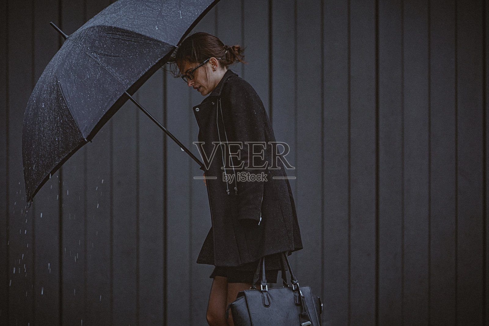 一名年轻女子撑着伞，在寒冷的秋日里在风雨中行走。照片摄影图片