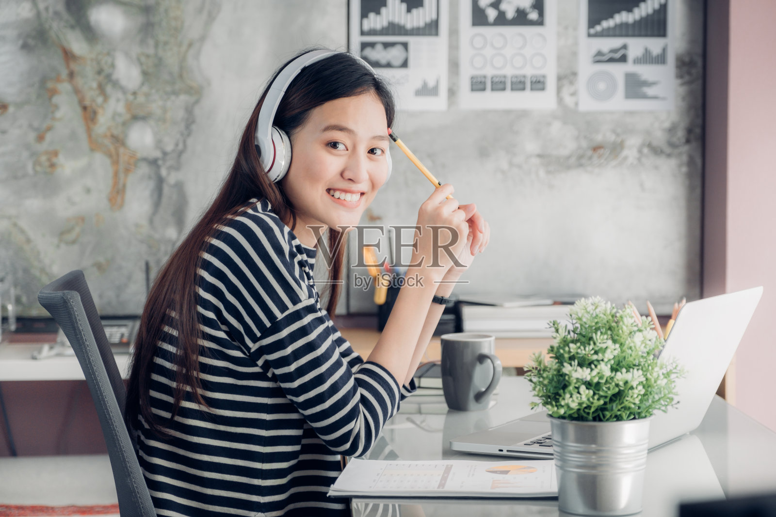 年轻的亚洲休闲女商人手臂上的桌子休息姿势与笔记本电脑和听音乐通过耳机思考工作，工作在家里与放松的感觉概念照片摄影图片