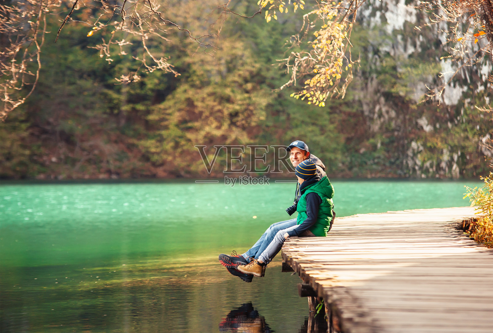 父子俩坐在湖上的木桥上照片摄影图片