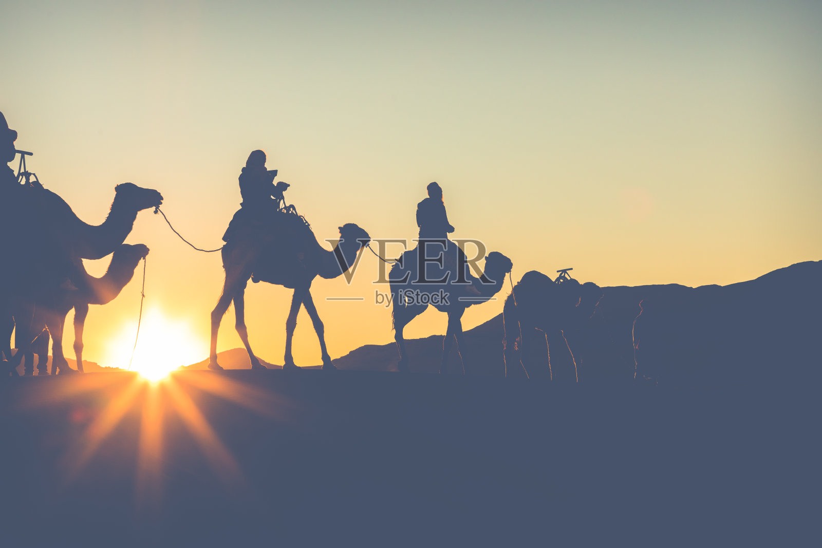 骆驼商队和人们一起穿过撒哈拉沙漠的沙丘。摩洛哥、非洲。照片摄影图片