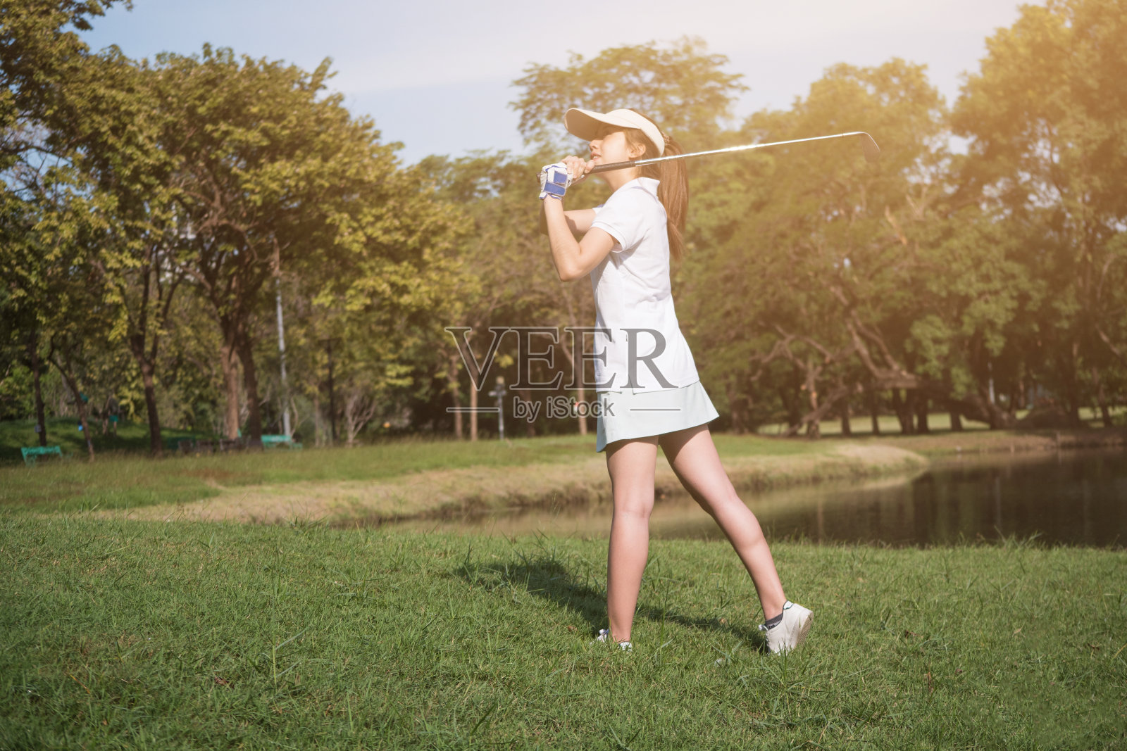 亚洲女子高尔夫球运动员挥杆驾驶高尔夫球俱乐部在高尔夫球场。照片摄影图片