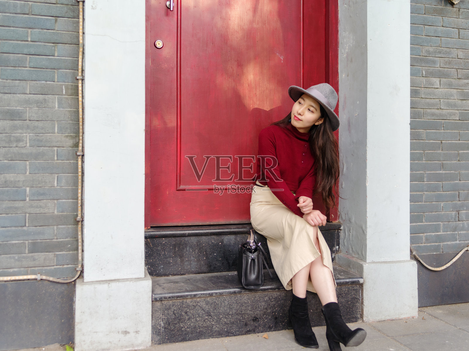 美丽的中国人坐在一扇红色大门前的台阶上，等着有人回家。照片摄影图片
