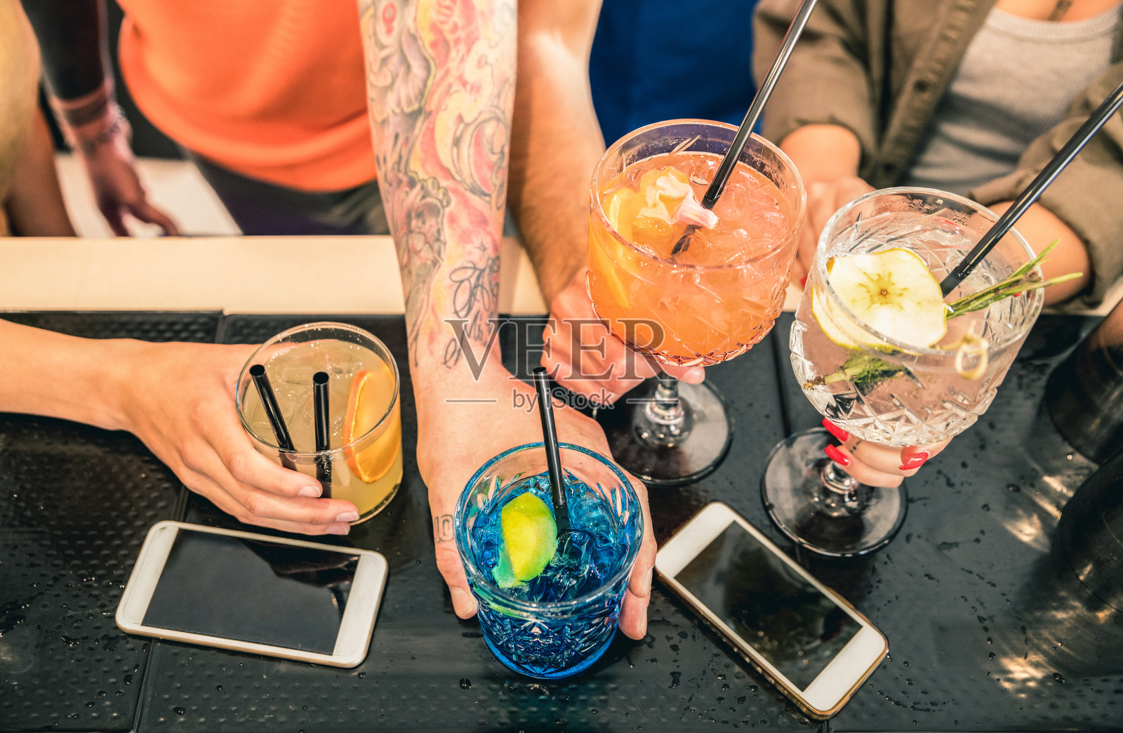朋友群喝鸡尾酒在时尚酒吧餐厅-高角度的观点，人的手在移动智能手机-社会聚集概念与喝醉的男孩和女孩-生动的蓝绿色滤镜照片摄影图片