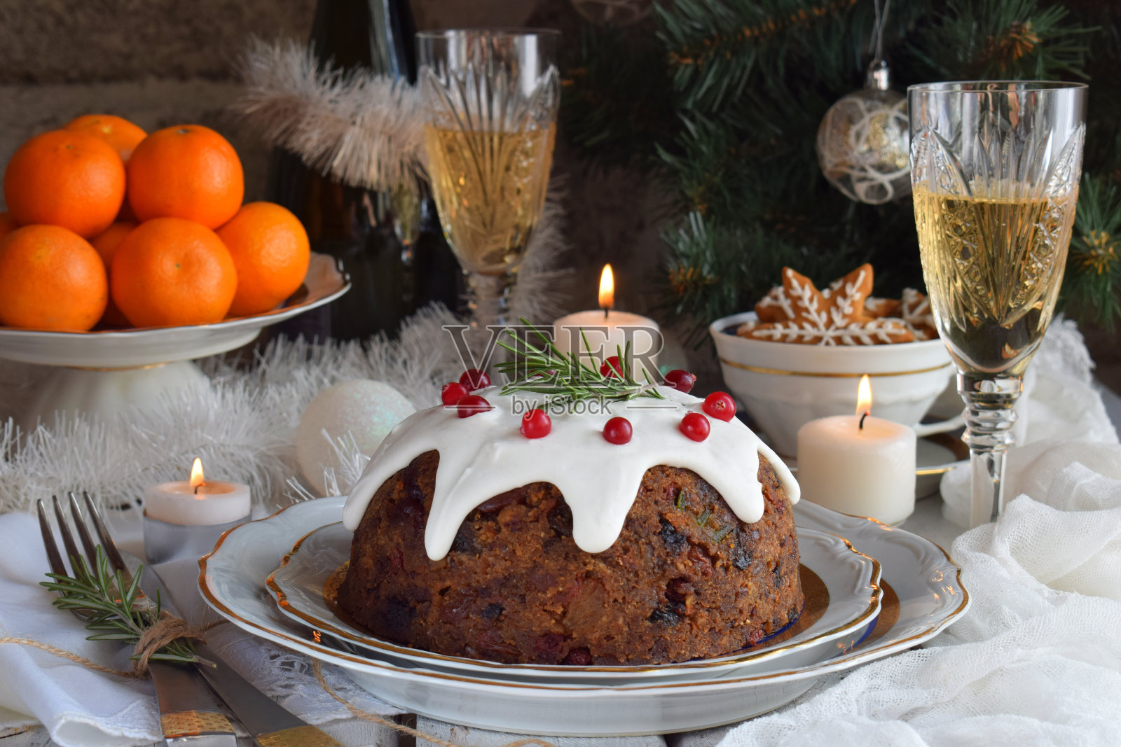 传统的英国圣诞蒸布丁与冬天的浆果，干果，坚果在节日设置与圣诞树，燃烧的蜡烛，橘子和一杯白葡萄酒，香槟。水果蛋糕照片摄影图片
