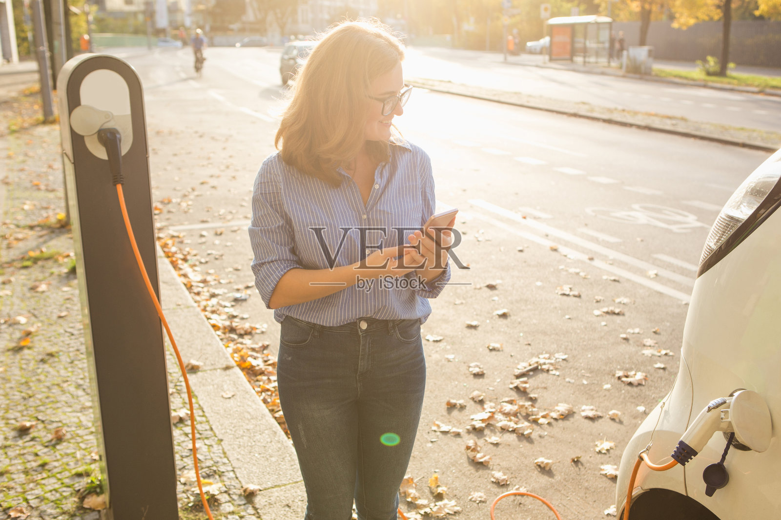 年轻女子站在电动汽车附近，手里拿着智能手机照片摄影图片