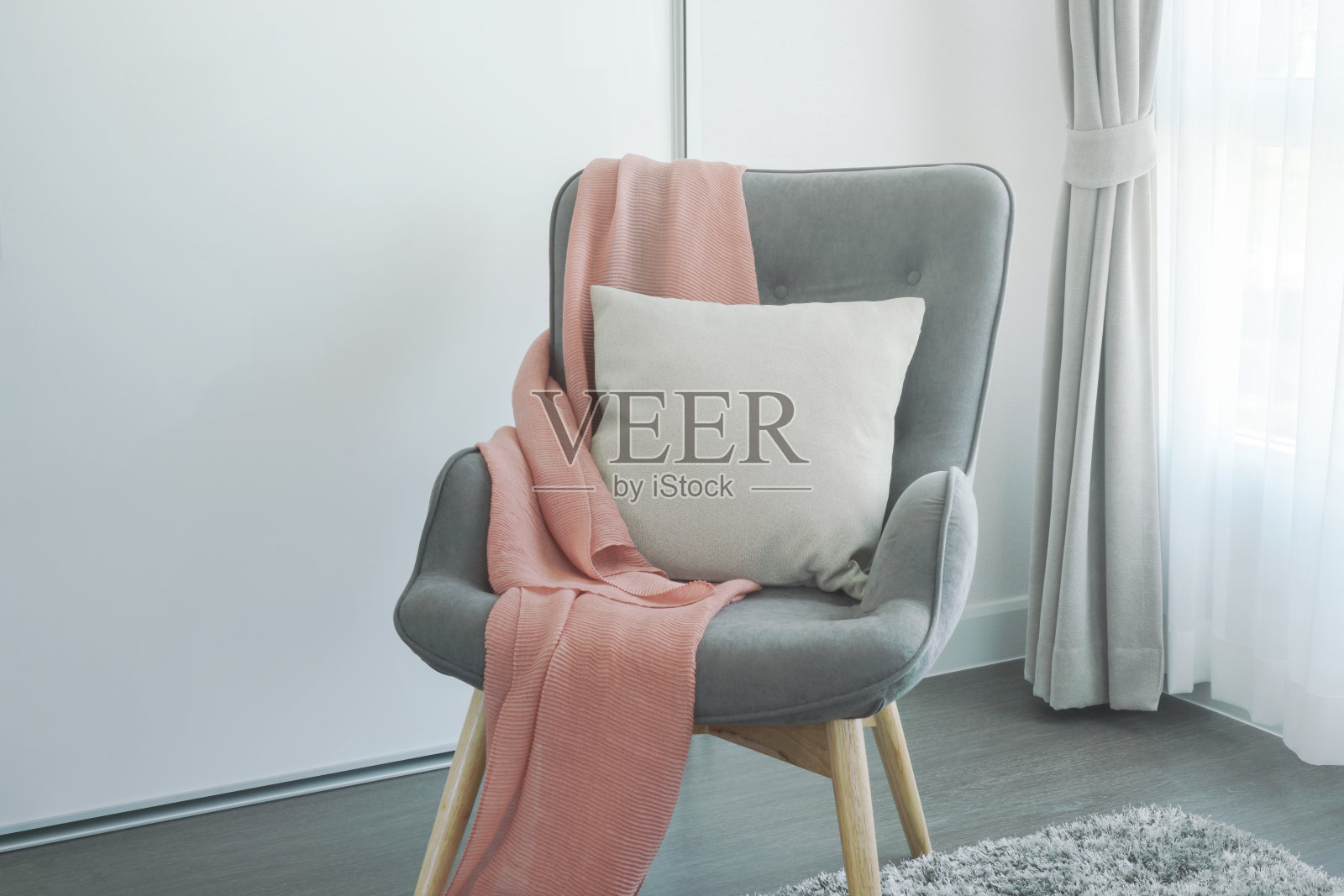 粉红色的围巾和米色的枕头放在客厅角落的灰色扶手椅上照片摄影图片