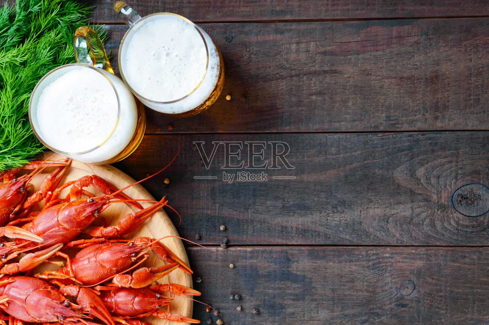 一堆美味的煮小龙虾放在一个圆形的木托盘上，两杯冰啤酒放在深色的背景上。前视图。为题字预留空间。照片摄影图片