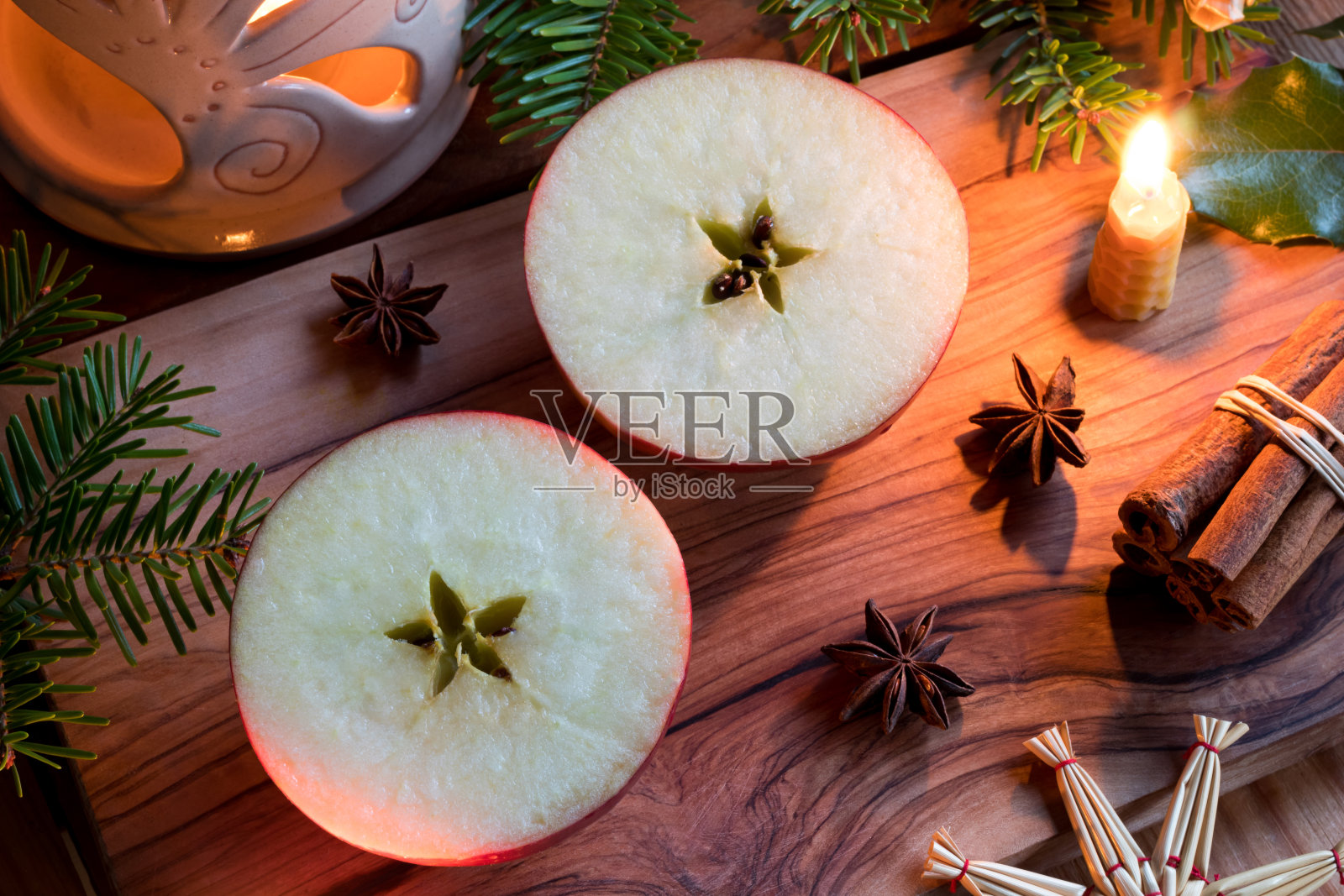 圣诞装饰-切成一半的苹果，一支蜡烛，肉桂棒，八角，杉木枝，和一个香味灯照片摄影图片