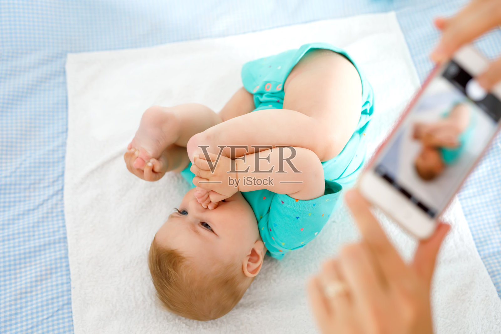 父母用智能手机给宝宝拍照。萌萌的新生宝宝把脚放在嘴里照片摄影图片