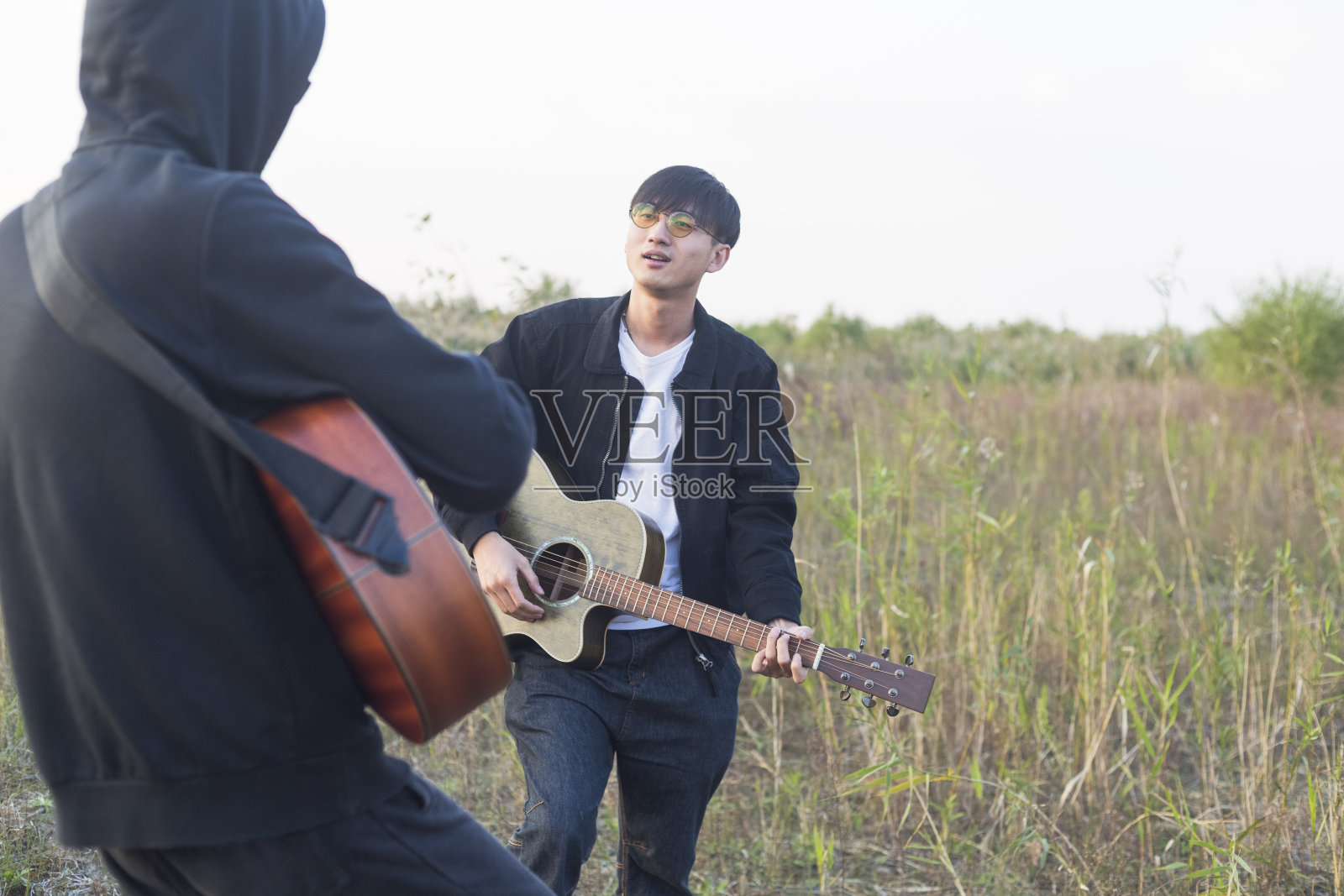 两个男人，朋友在草地上练习原声吉他照片摄影图片
