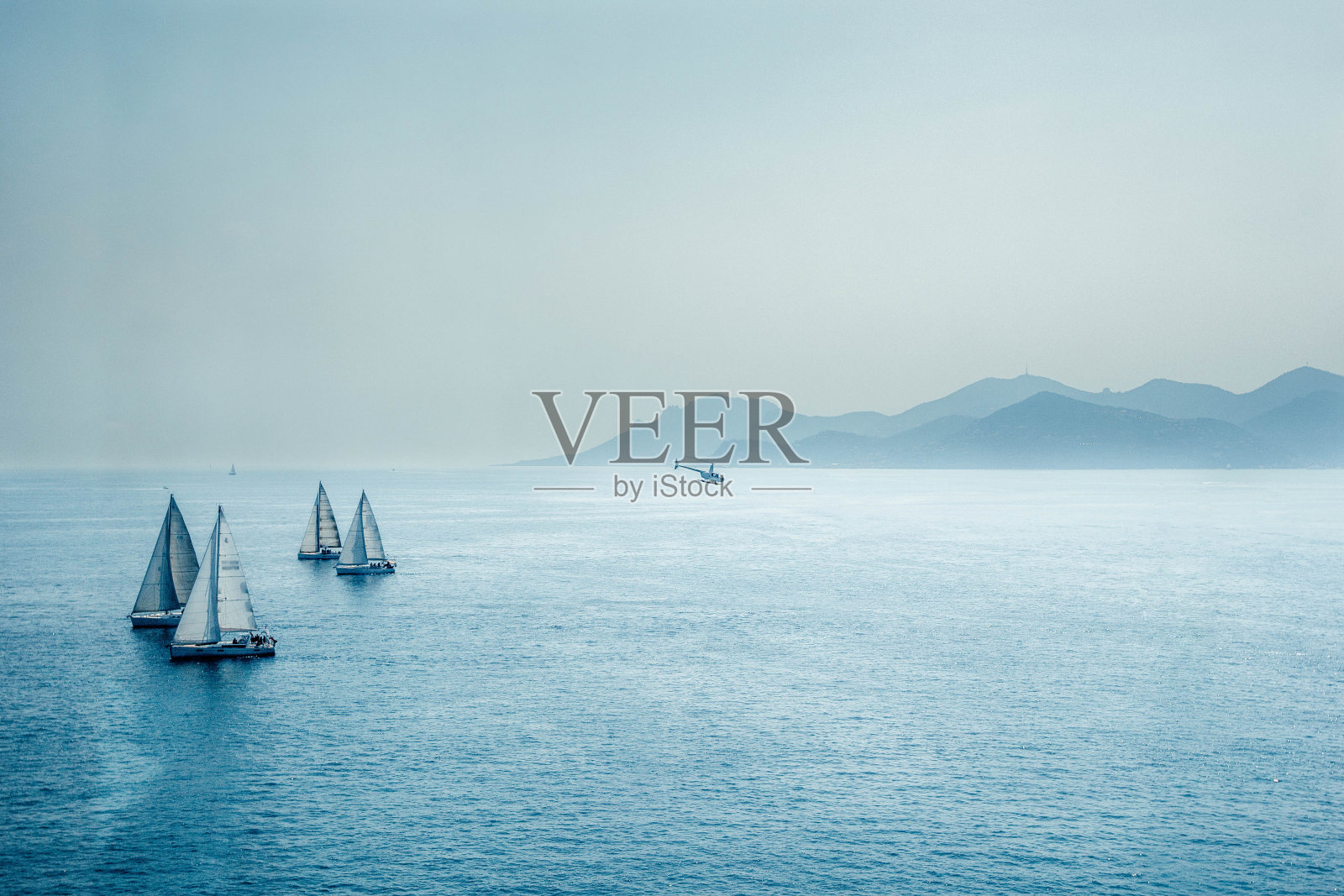帆船比赛或一组小型水上比赛船和直升机在地中海，与蓝山在地平线上的全景照片摄影图片