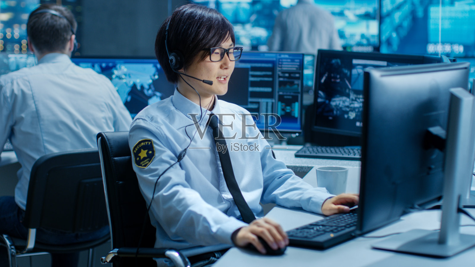 在安全指挥中心，工作站上的官员监视屏幕并通过耳机与巡逻人员通信。他是监视小组的一员。照片摄影图片