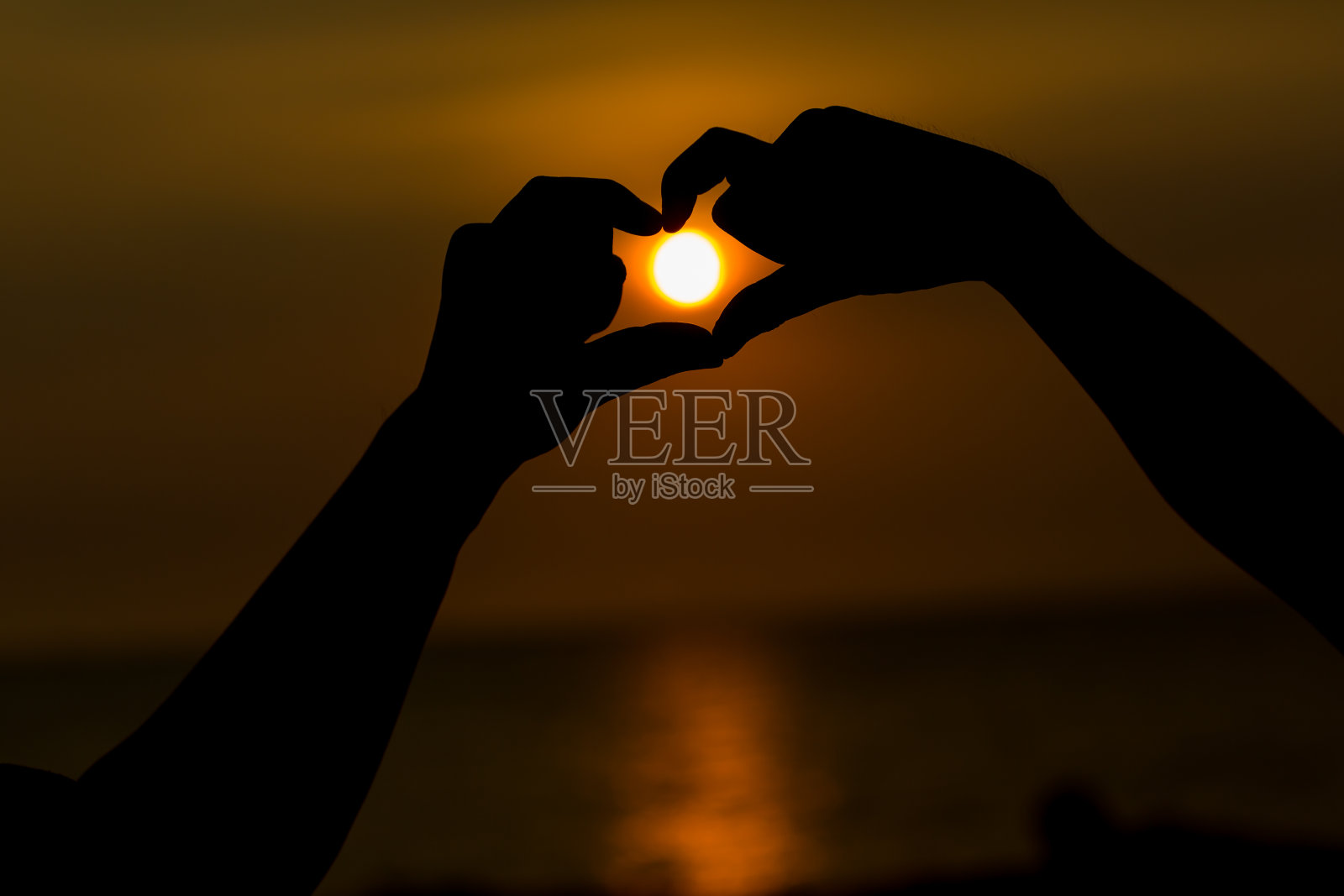 手的剪影，使一个心形的象征与美丽的日落背景。照片摄影图片