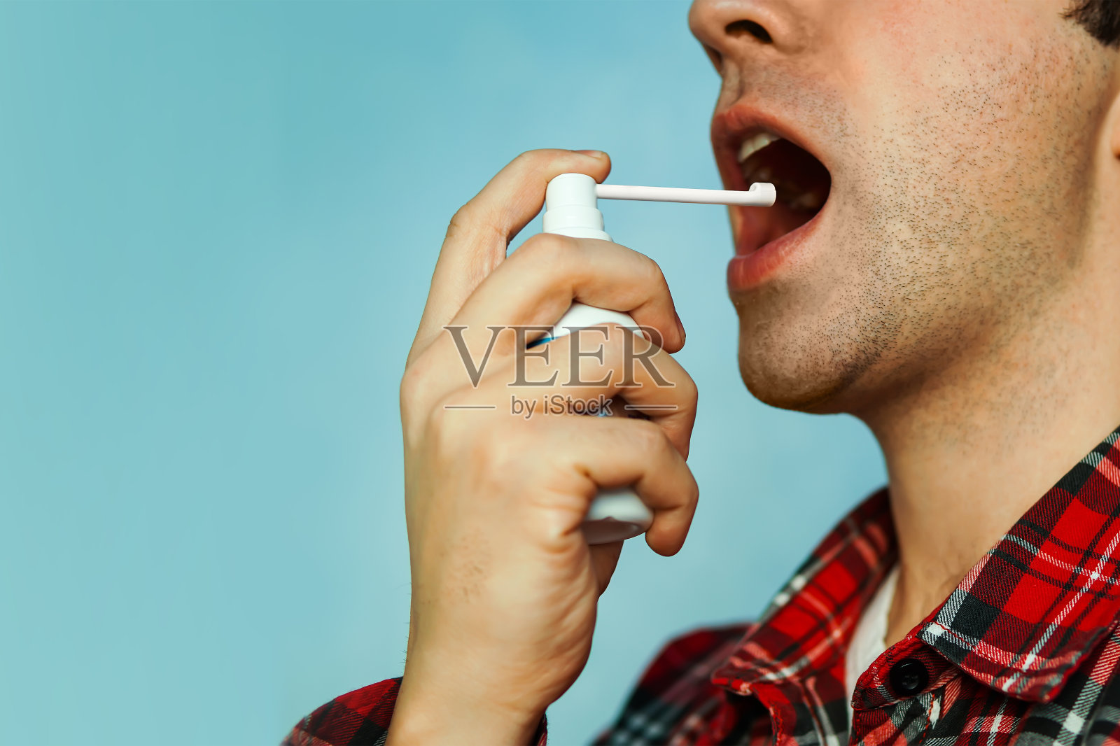 一个生病的年轻人用喷喉剂喷彩色背景照片摄影图片