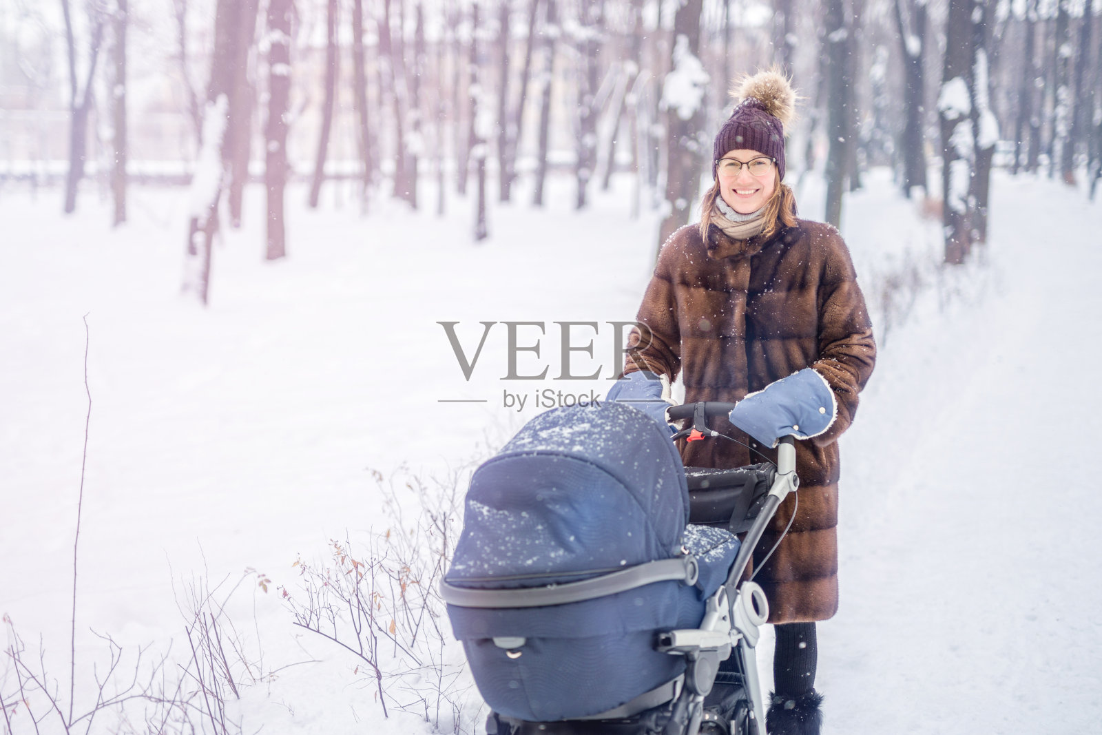 一个女人在冬天的森林里推着婴儿车。照片摄影图片
