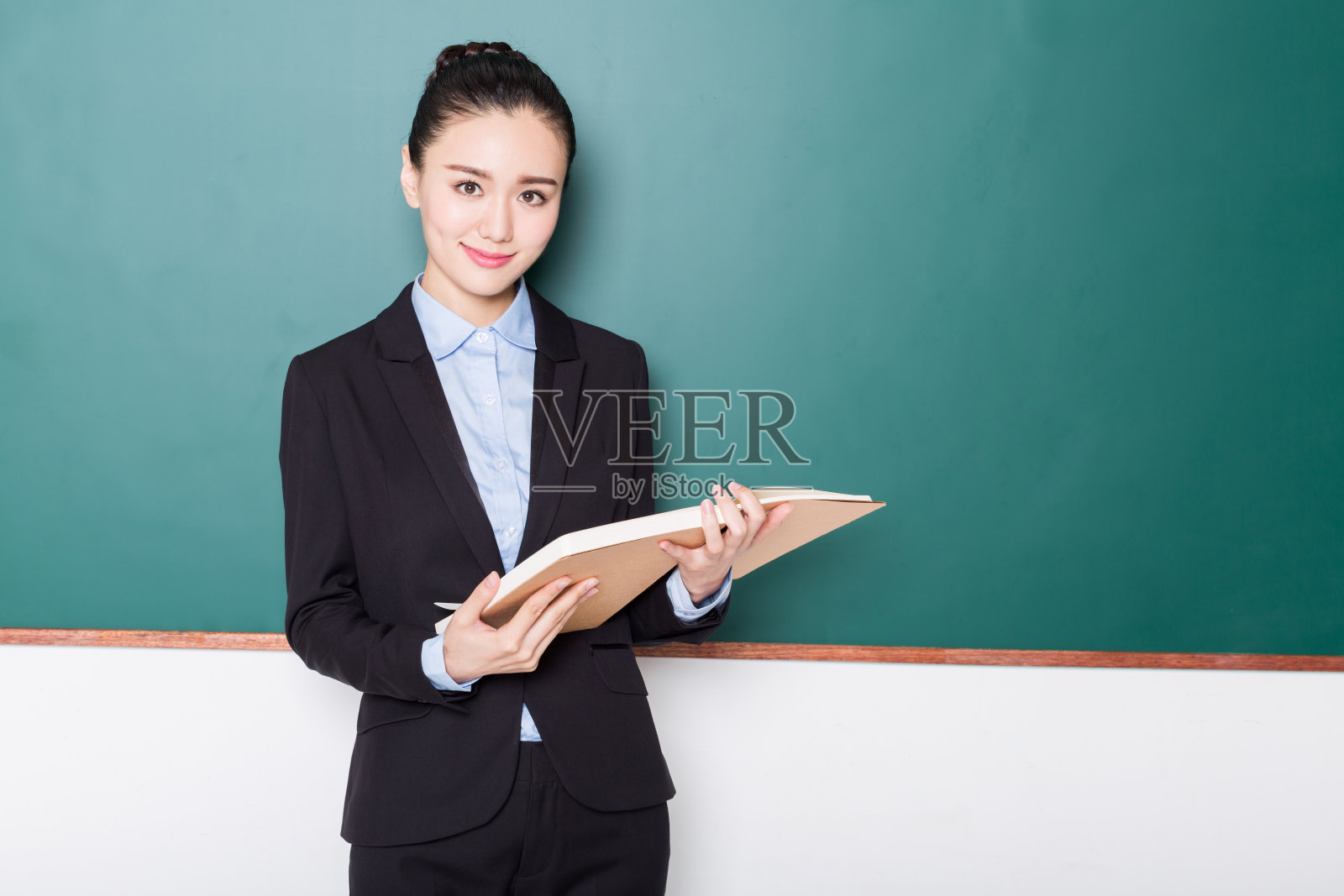 女老师拿着书在黑板前照片摄影图片