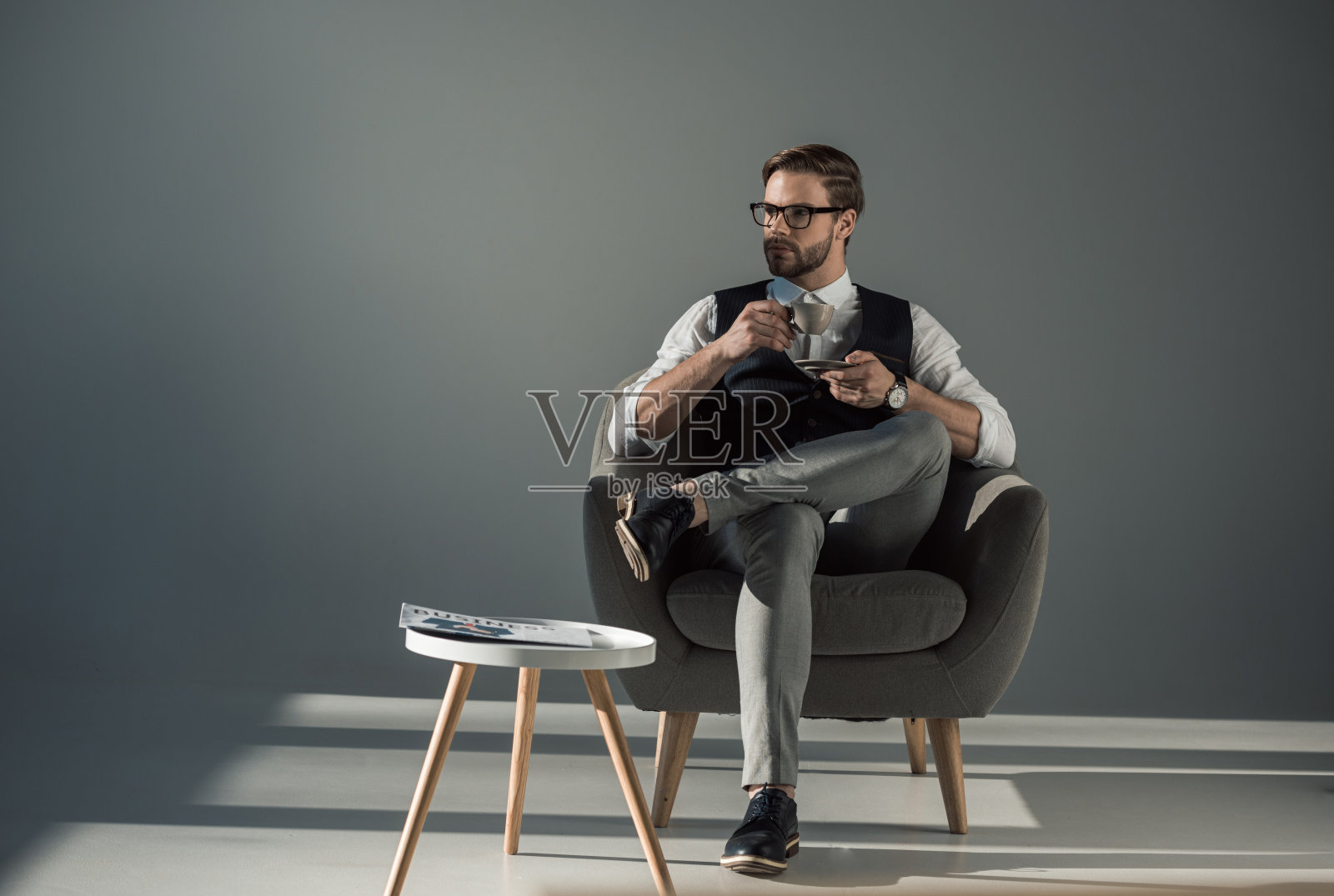 英俊潇洒的年轻人坐在扶手椅上，一边喝咖啡一边看别处照片摄影图片