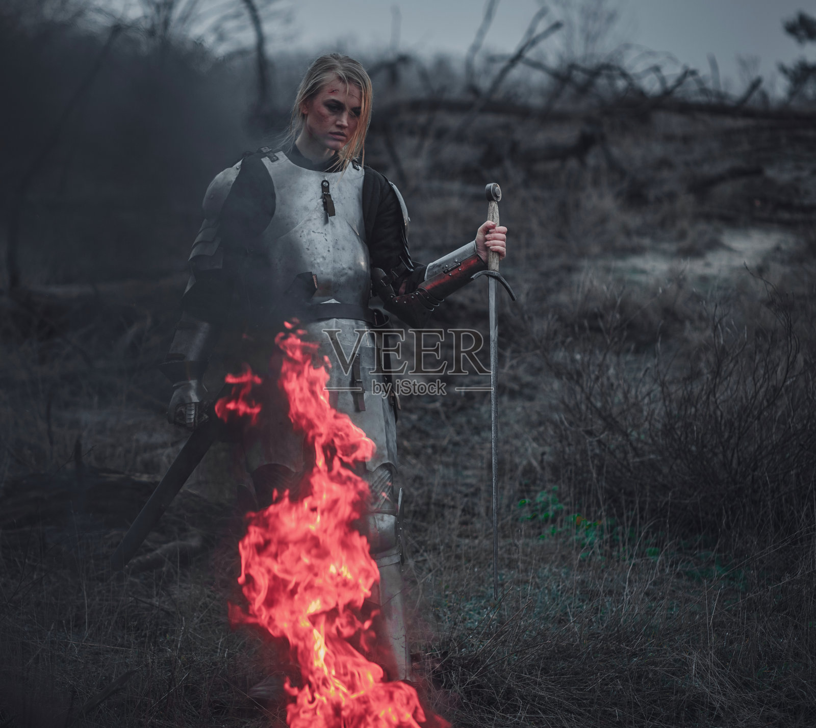 《贞德》中的女孩身穿铠甲，手持利剑，背景是火和烟。照片摄影图片