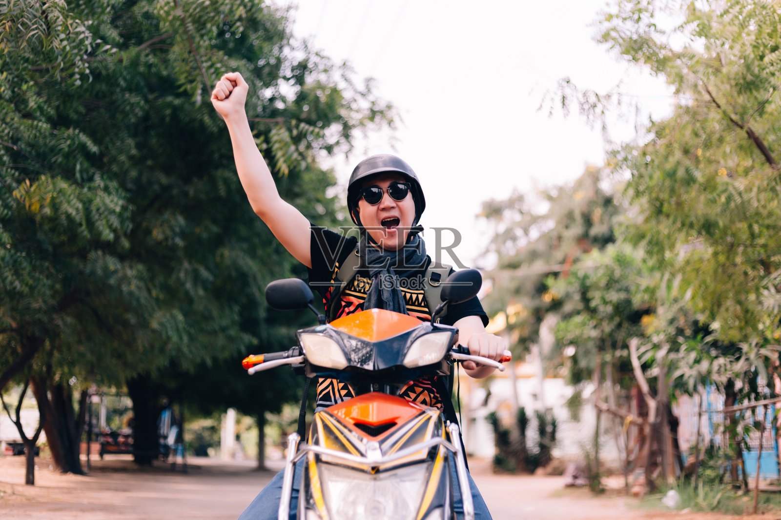 戴着墨镜和头盔骑着摩托车的年轻人举起双手，表示胜利和成功。照片摄影图片