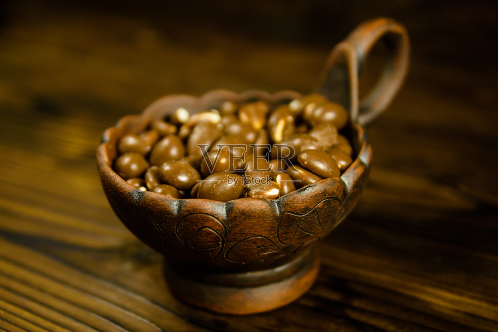 木桌上的陶瓷碗里装着巧克力釉的花生照片摄影图片